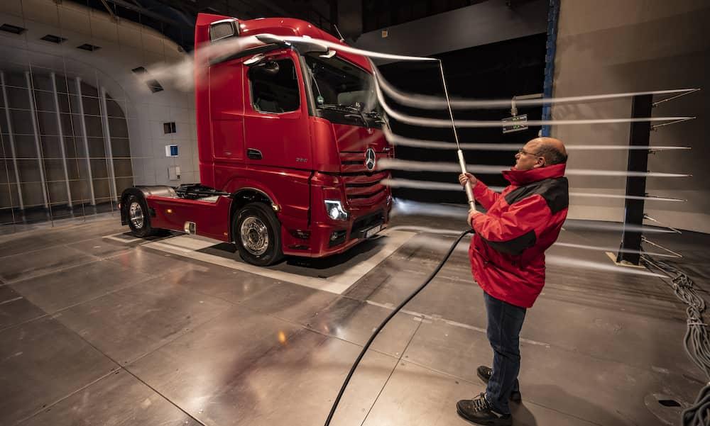 Perspective view of a red lorry cabin in an open section wind tunnel with oncoming air visualised with smoke