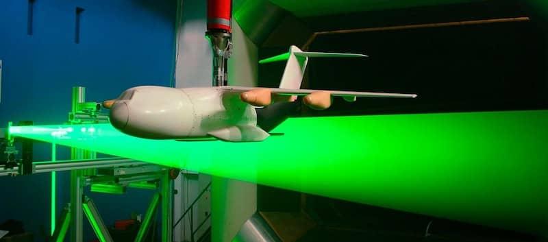 A white aircraft wind tunnel model suspended above a green laser sheet
