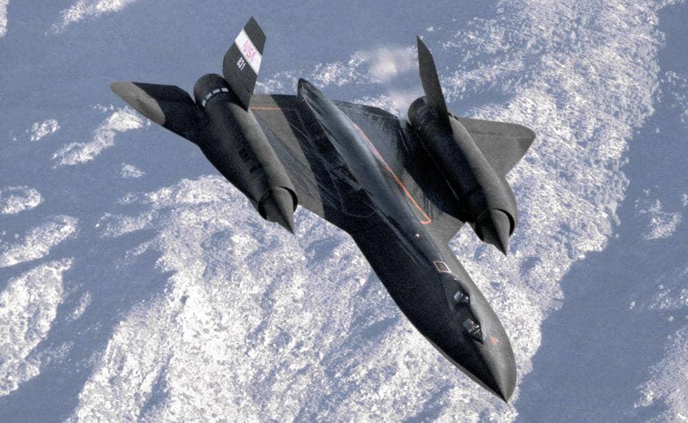A dark grey SR-71 flying over mountains